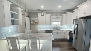 Una cocina moderna con armarios blancos, una isla con encimera de mármol y un refrigerador de acero inoxidable.
