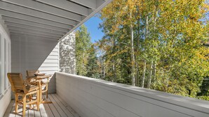 A wooden deck with a table and chairs, overlooking a forest with autumn foliage.