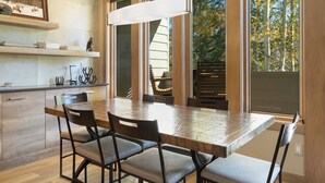 A modern kitchen with a large wooden table, four chairs, and a hanging light fixture.