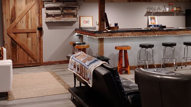 A rustic bar area with wooden beams, a large wooden door, and a bar counter with stools. - Pet Friendly, Scenic, Eureka, St Louis, Nurse, Insurance, Contractor spec. rates (High Ridge)
