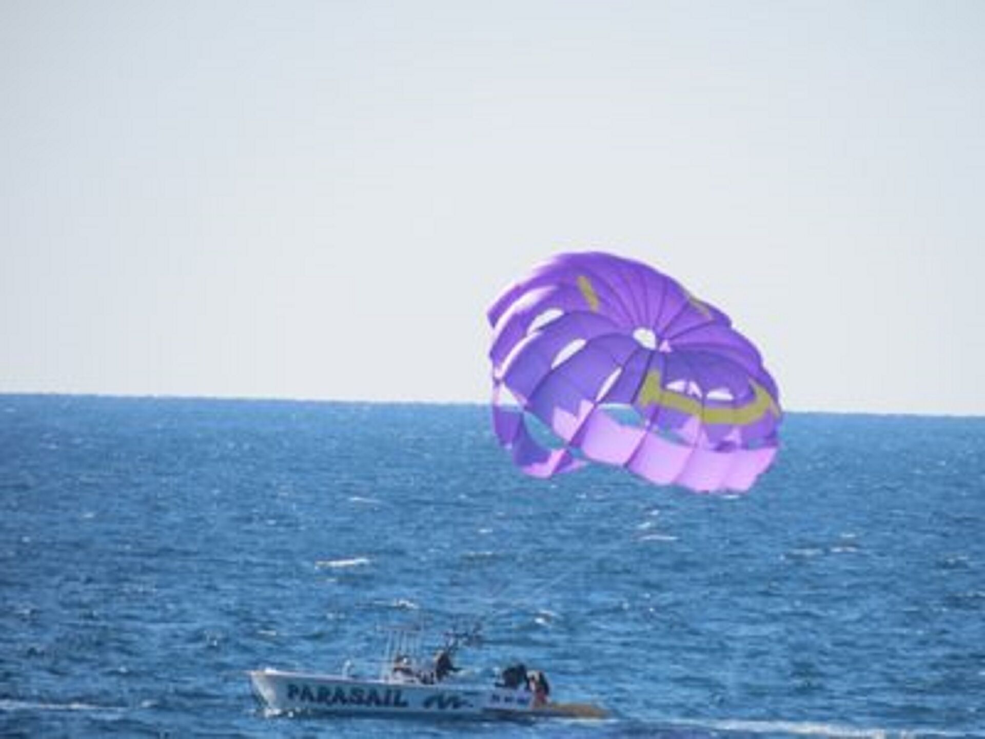 A parasail with purple and yellow colors over a body of water.
