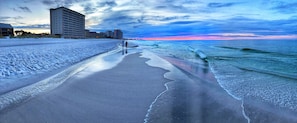 A beach with a long, narrow path leading to the water, surrounded by buildings.