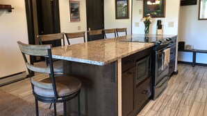 A kitchen with a central island, wooden chairs, pendant lighting, and framed artwork on the walls. - Remodeled ski in/ski out condo in Mt Crested Butte with incredible views! (Crested Butte)