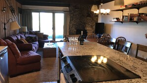 A modern kitchen with a large island, a stone wall, and a dining area with wooden chairs. - Remodeled ski in/ski out condo in Mt Crested Butte with incredible views! (Crested Butte)