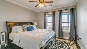 A bedroom with a bed, a ceiling fan, a heater, a window with curtains, and a view of the outside.