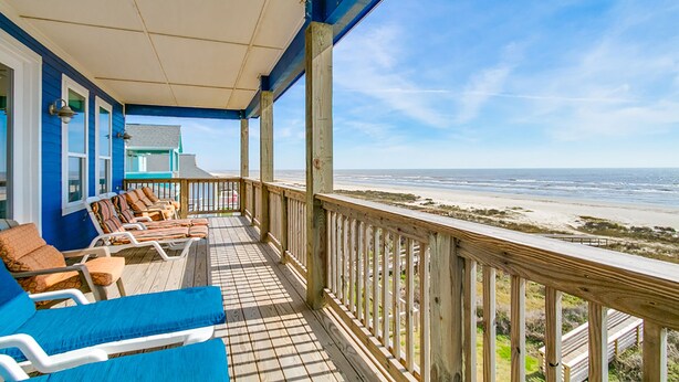 A covered deck with lounge chairs and a view of the beach.