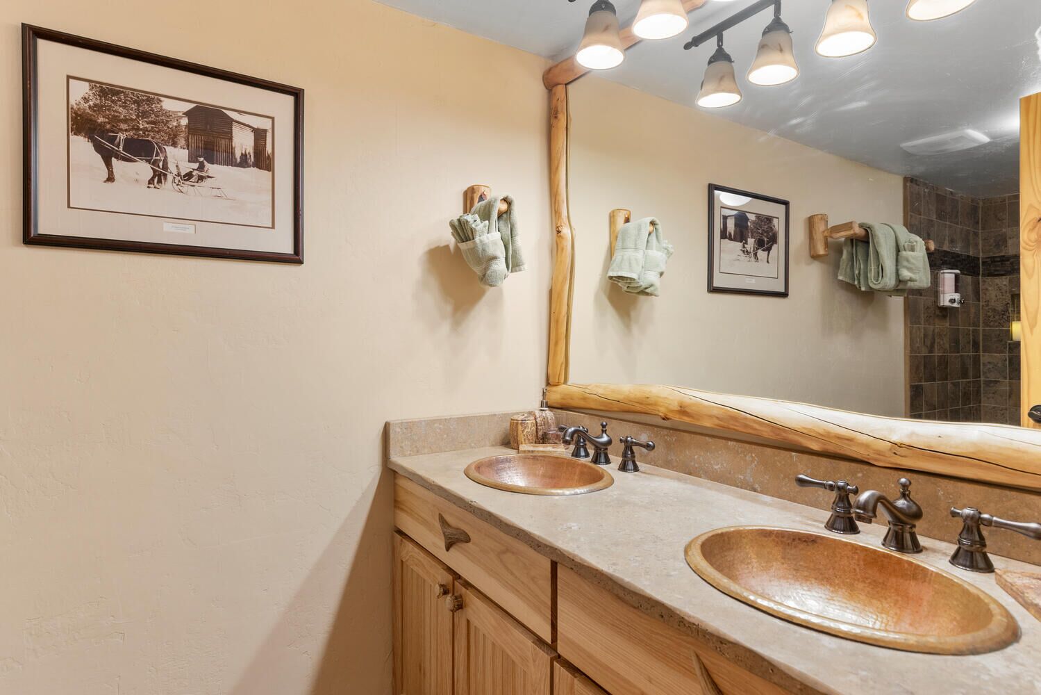 A bathroom with two sinks, wooden cabinets, a large mirror, and a framed historical photo on the wall.