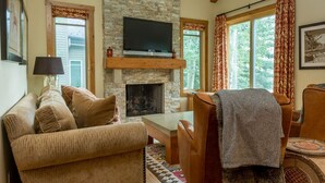 A cozy living room with a stone fireplace, a flat-screen TV mounted above it, a sofa, and a coffee table. - Fairway Nine Town Home Retreat Sun Valley (Sun Valley)