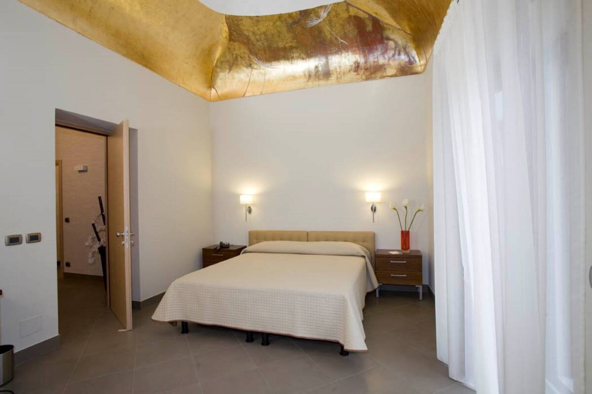 A bedroom with a bed, bedside tables, a nightstand, a door, and a curtain.