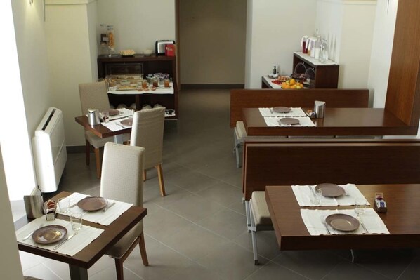 Une salle à manger avec plusieurs tables dressées pour les repas, un coin cuisine à l’arrière-plan et une vue sur la salle à manger à travers une porte.