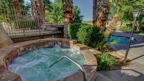 A hot tub surrounded by palm trees and a pool, with a stone wall and a metal fence in the background. - Las Palmas Spectacular View-Elevator, Washer-Dryer, No Resort Fees - Great RATE! (St George)
