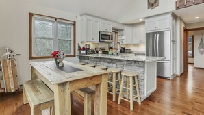 A kitchen with white cabinets, a stone island, a wooden table with stools, and a mounted deer head.