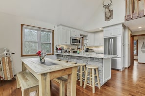 A kitchen with white cabinets, a stone island, a wooden table with stools, and a mounted deer head.