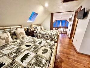 Une chambre avec deux lits, une tête de lit en bois, une table de chevet et un téléviseur fixé au mur.