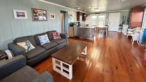 Ein gemütliches Wohnzimmer mit einer grauen Couch, einem Holztisch und einer Küche im Hintergrund.