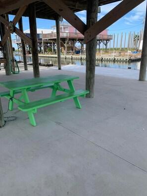 Une table de pique-nique verte, placée sous une structure en bois, au bord de l’eau.