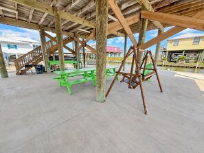 An outdoor pavilion with picnic tables and a swing set, supported by wooden beams. - Wahoo: Coastal Realty Group (GRAND ISLE)
