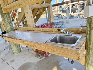 A wooden outdoor kitchen with a stainless steel sink and a metal rack. - Wahoo: Coastal Realty Group (GRAND ISLE)