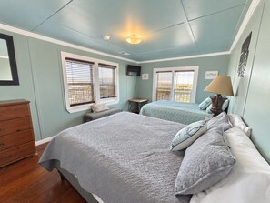 A bedroom with two beds, a dresser, a nightstand, a lamp, and a ceiling fan. - Wahoo: Coastal Realty Group (GRAND ISLE)