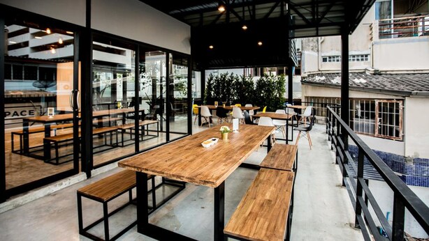 An indoor dining area with wooden tables and benches, large windows, and a view of the cityscape. - The CAPSULE by UnionSPACE - Adults Only (Bangkok)