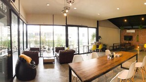 A spacious indoor area with a long wooden table, several chairs, and a sofa. There are large windows allowing natural light and views of greenery outside. - The CAPSULE by UnionSPACE - Adults Only (Bangkok)