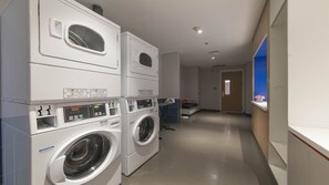 A laundry area with stacked washing machines and dryers, a bench, and a reception desk with a blue accent wall. - Holiday Inn Express Liyang Huafu by IHG (Changzhou)
