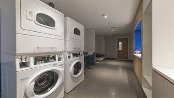 Zona de lavandería con lavadoras y secadoras apiladas, una banca y un mostrador de recepción con una pared azul decorativa.