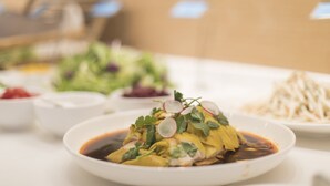 A table with a dish of food garnished with herbs and a sauce, surrounded by other dishes and bowls. - Holiday Inn Express Liyang Huafu by IHG (Changzhou)