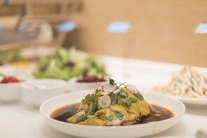 A table with a dish of food garnished with herbs and a sauce, surrounded by other dishes and bowls.