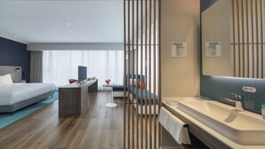 A modern hotel room with a bed, a desk, a sofa, a bathroom with a large mirror, and a view of the city. - Holiday Inn Express Liyang Huafu by IHG (Changzhou)