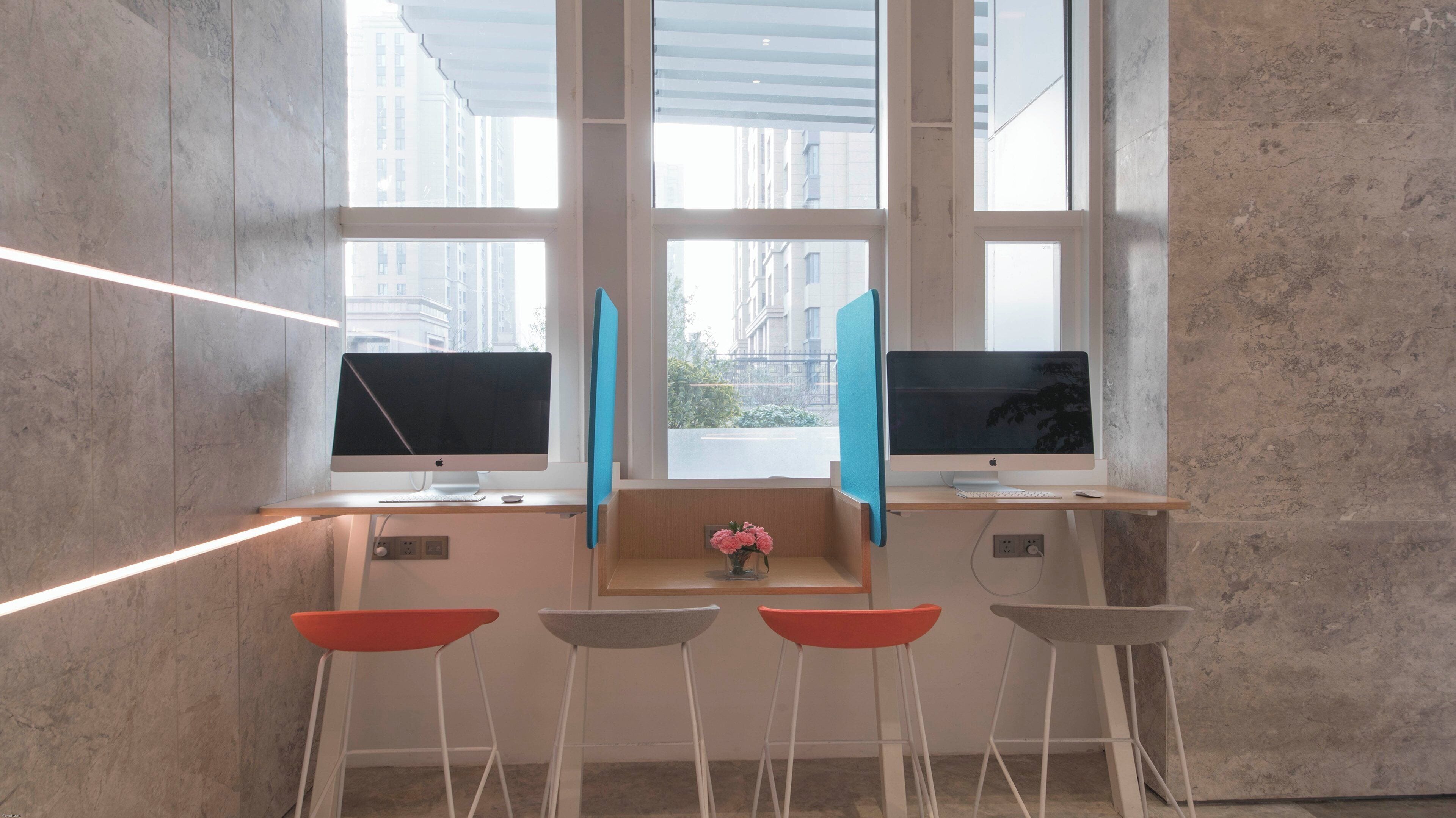 Un espace de travail moderne avec deux écrans, un clavier et une souris sur un bureau en bois. On y trouve quatre chaises et un vase avec des fleurs posé sur le bureau.