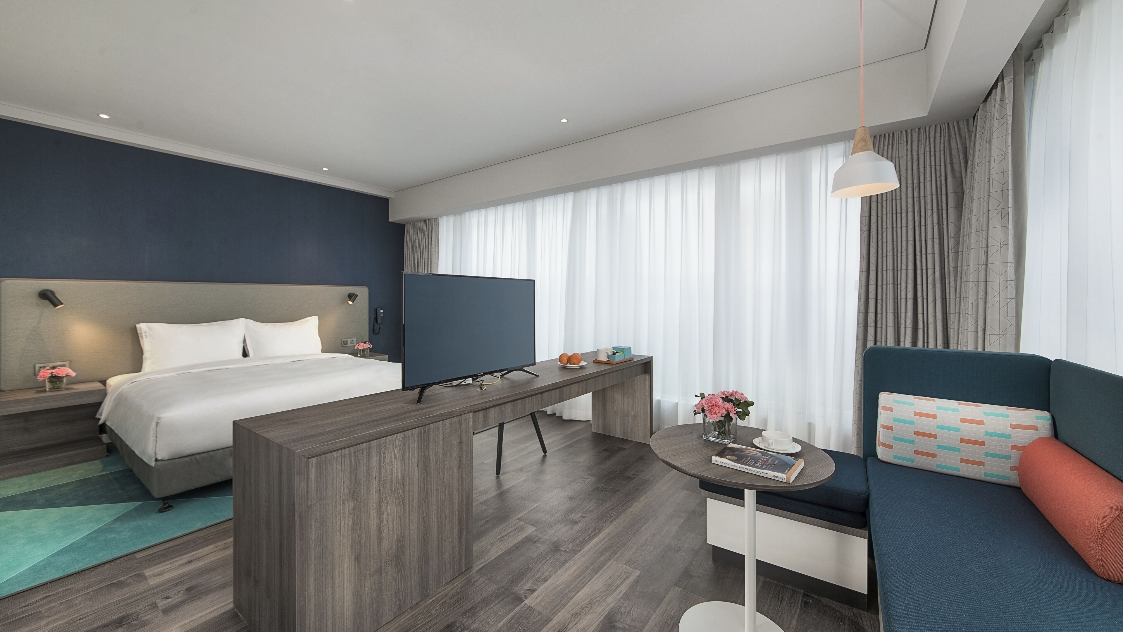 A modern hotel room with a bed, a desk, a TV, and a sofa.