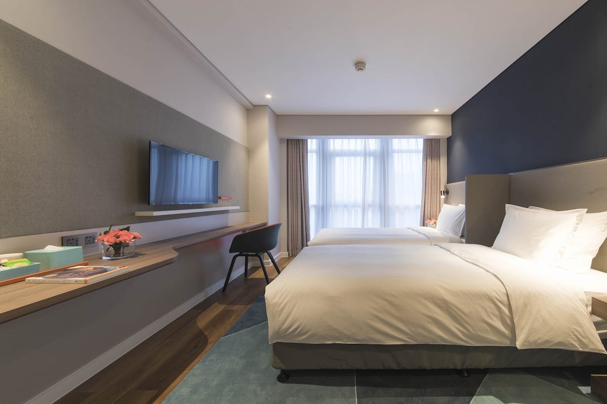 Ein modernes Hotelzimmer mit einem großen Bett, einem an der Wand befestigten Fernseher, einem Schreibtisch mit Stuhl und einem fenster mit Vorhängen.