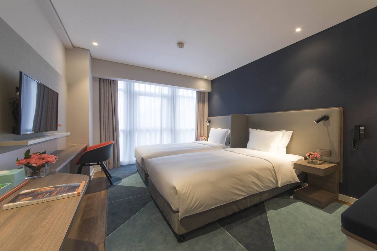 Ein Hotelzimmer mit einem großen Bett, Nachttischen, einem Schreibtisch, einem Fernseher und einem Fenster mit Vorhängen.
