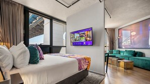 A modern hotel room with a large bed, a TV mounted on the wall, a green sofa, and a view of a bridge outside the window. - Crystalbrook Vincent (Brisbane)