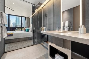 A modern hotel room with a glass shower enclosure, a large mirror, and a bed with a city view. - Crystalbrook Vincent (Brisbane)