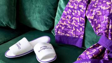 Un sofá verde con una manta morada estampada y pantuflas blancas con texto.
