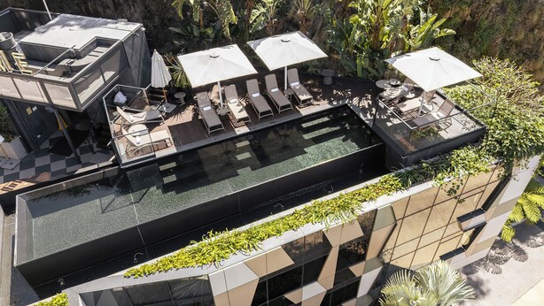 A rooftop infinity pool with lounge chairs and umbrellas, surrounded by greenery and modern architecture. - Crystalbrook Vincent (Brisbane)