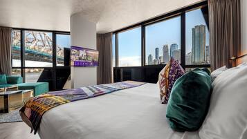 A hotel room with a large bed, a TV, a desk, and a view of a cityscape.