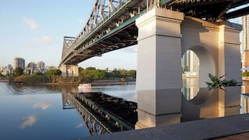 A bridge with a reflection in the water, a cityscape in the background, and a clear sky.
