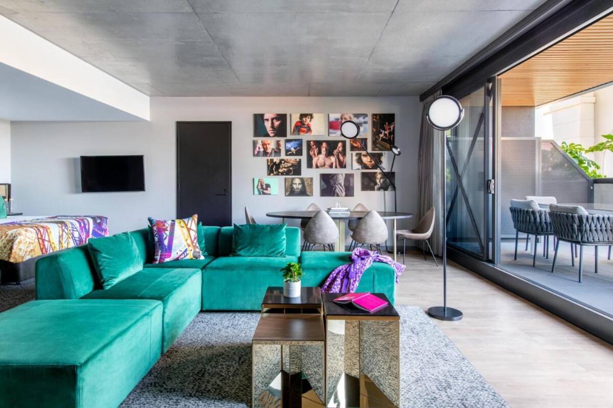Un salon moderne avec un canapé vert, une table basse et un mur décoré de différents tableaux.