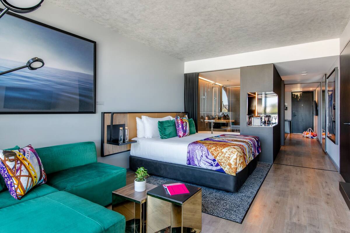 Une chambre d’hôtel moderne avec un grand lit, un canapé vert, une petite table et une grande fenêtre.