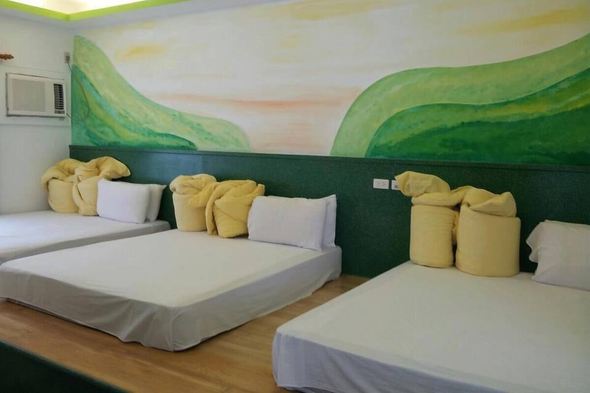 A hotel room with two beds, each with a green headboard and white bedding. There is a large wall mural depicting a landscape.