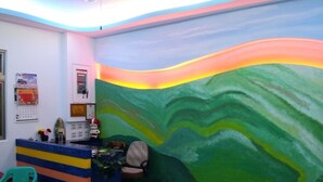 Un área de recepción con un mostrador colorido, una silla y un mural en la pared.
