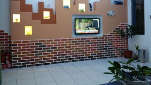Una sala de estar moderna con un televisor montado en una pared de ladrillo, luces decorativas y una planta en maceta.