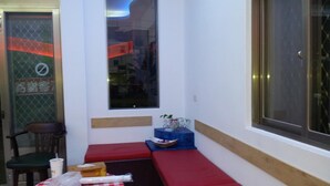 Una habitación pequeña con una mesa a cuadros, un banco rojo, una silla y una ventana con vista a la calle.