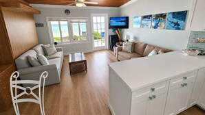 Un salon avec un plafond en bois, un téléviseur et une vue sur l’océan grâce à de grandes fenêtres.