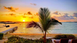 Une vue sur le coucher de soleil, avec un palmier, une plage et des chaises longues.