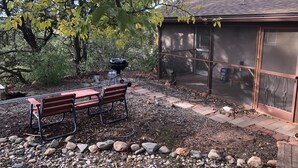 Une terrasse avec un barbecue, deux bancs et un espace abrité doté d’une fenêtre.