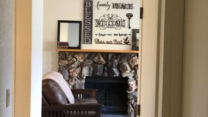Un salon chaleureux avec une cheminée en pierre, un canapé en cuir et une pancarte de bienvenue au-dessus de la cheminée.